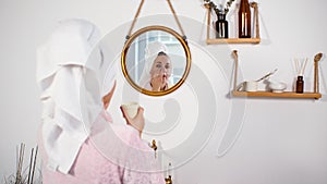 Woman Putting Creme on Face in Front of Mirror