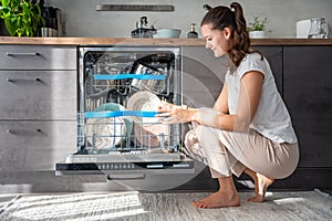 A woman putting dirty ceramic dish in the dishwasher. Household and helpful technology concept