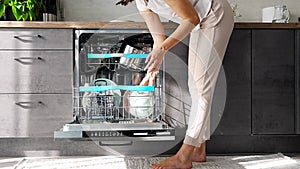 A woman putting dirty ceramic dish in the dishwasher. Household and helpful technology concept