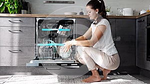 A woman putting dirty ceramic dish in dishwasher. Household and helpful technology concept