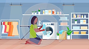 Woman putting dirty clothes into washing machine african american housewife doing housework modern laundry room interior