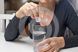 woman is putting an effervescent vitamin tablet into a glass of water