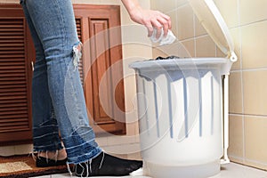 Woman putting empty plastic bag in recycling bin in the kitchen.