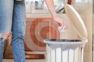 Woman putting empty plastic bag in recycling bin in the kitchen.