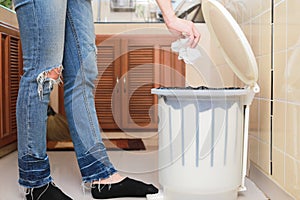 Woman putting empty plastic bag in recycling bin in the kitchen.