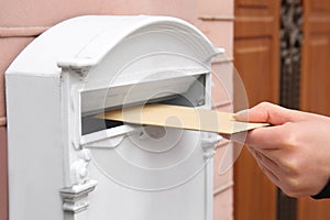 Woman putting envelope into mailbox on wall of building outdoors