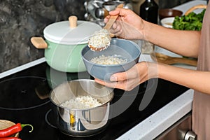 Woman putting freshly cooked rice into bowl in kitchen