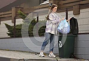 Woman putting garbage bag into recycling bin outdoors