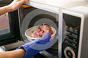 Woman putting grilled pork into microwave oven. inside view photo
