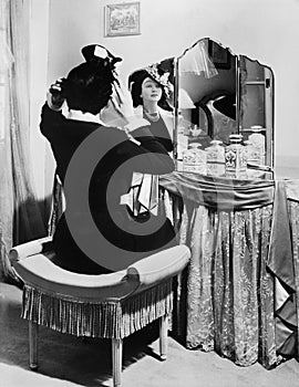 Woman putting on a hat in front of a dressing table