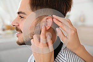 Woman putting hearing aid in man`s ear indoors