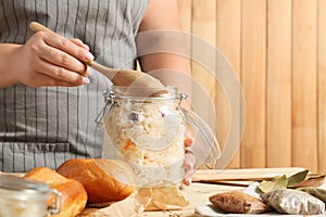Woman putting homemade sauerkraut into glass jar at table