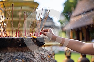 A woman putting the incense sticks in the incense burner after making a wish at a temple