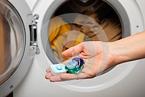 Woman putting laundry detergent capsule into washing machine indoors, closeup.