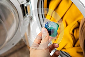 Woman putting laundry detergent capsule into washing machine indoors, closeup.