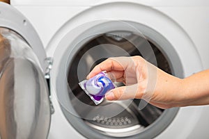 Woman putting laundry detergent capsule into washing machine indoors, closeup.