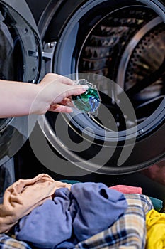 Woman putting laundry detergent capsule into washing machine indoors, closeup. Washing clothes.The concept of washing