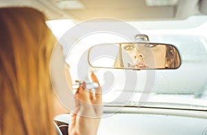 Woman putting lipstick in the car.