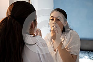 Woman putting lipstick on her lips in a room. Doing make up. Looking at the mirror