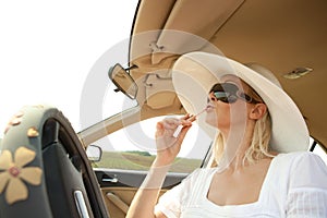 Woman putting lipstick on using the car mirror