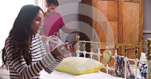 Woman Putting On Make Up And Man Getting Dressed In Bedroom