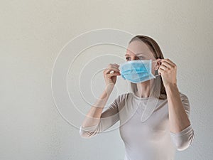 A woman putting on a medical disposable mask to avoid contagious viruses