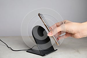 Woman putting mobile phone onto wireless charger at  grey table, closeup