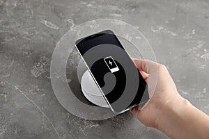 Woman putting mobile phone onto wireless charger at  grey table, closeup
