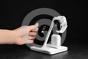 Woman putting mobile phone onto wireless charger at  stone table, closeup