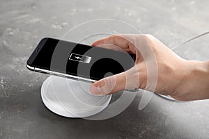 Woman putting mobile phone onto wireless charger at table, closeup