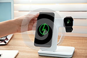 Woman putting mobile phone onto wireless charger at table, closeup. Modern workplace accessory