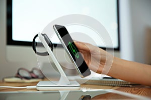 Woman putting mobile phone onto wireless charger at table, closeup. Modern workplace accessory