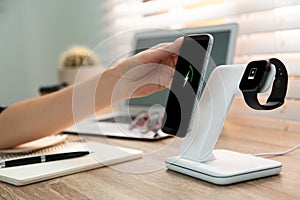 Woman putting mobile phone onto wireless charger at table, closeup. Modern workplace accessory