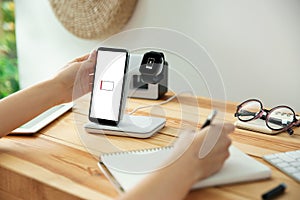 Woman putting mobile phone onto wireless charger at table, closeup. Modern workplace accessory