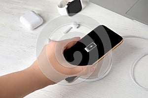 Woman putting mobile phone onto wireless charger at wooden table, closeup