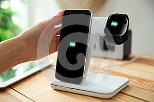 Woman putting mobile phone onto wireless charger at wooden table, closeup. Modern workplace accessory