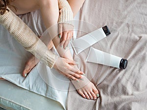 Woman putting or moisturizer cream on her legs. Skin care and health concept