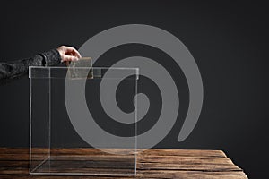 Woman putting money into donation box on table against grey background, closeup.