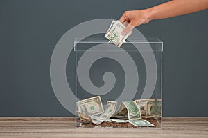 Woman putting money into donation box on table against grey background