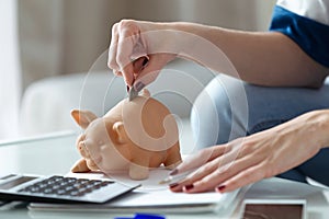 Woman putting money inside the piggy bank at home. Saving concept