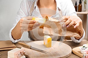 Woman putting natural handmade soap into bag at wooden table, closeup