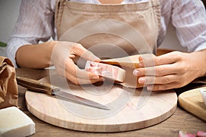 Woman putting natural handmade soap into paper bag at table, closeup
