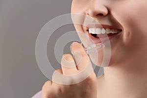 Woman putting occlusal splint in mouth on grey background, closeup photo