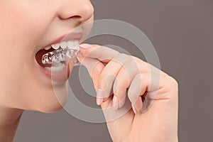 Woman putting occlusal splint in mouth on grey background, closeup photo