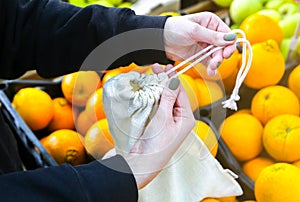 Woman is putting oranges in reusable shopping bag. Zero waste. Ecologically and environmentally friendly packets. Canvas and linen