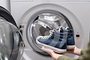 Woman putting pair of blue sneakers into washing machine, close up.