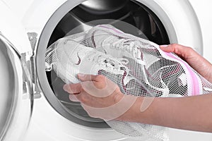 Woman putting pair of sport shoes in laundry bag into washing machine, closeup