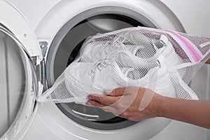 Woman putting pair of sport shoes in mesh laundry bag into washing machine, closeup