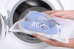 Woman putting pair of sport shoes in mesh laundry bag into washing machine, closeup