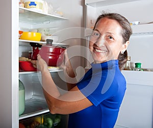 Woman putting pan into refrigerator